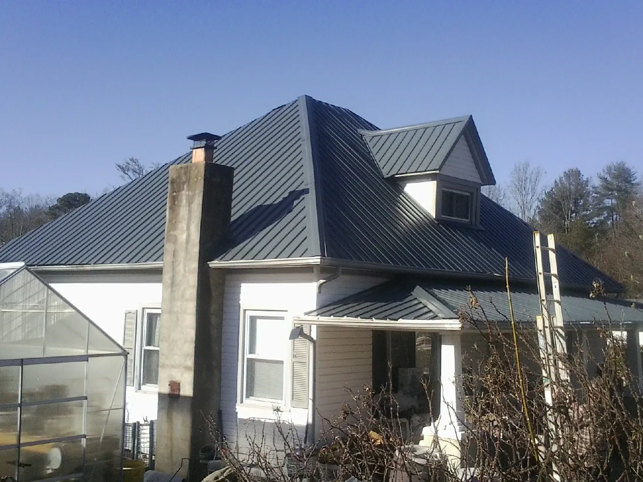 Dark blue standing seam metal roof on a white farmhouse with dormer — Slate & Tile Roof Repair by Roofing Brothers in Varysburg