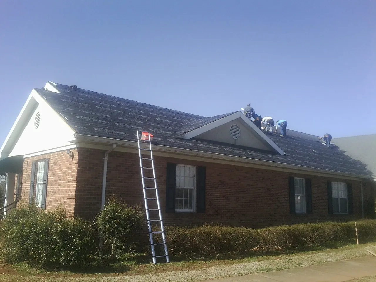 Crew tearing shingles off a brick ranch roof with a ladder set — Emergency Roof Repair work by our crew in Varysburg