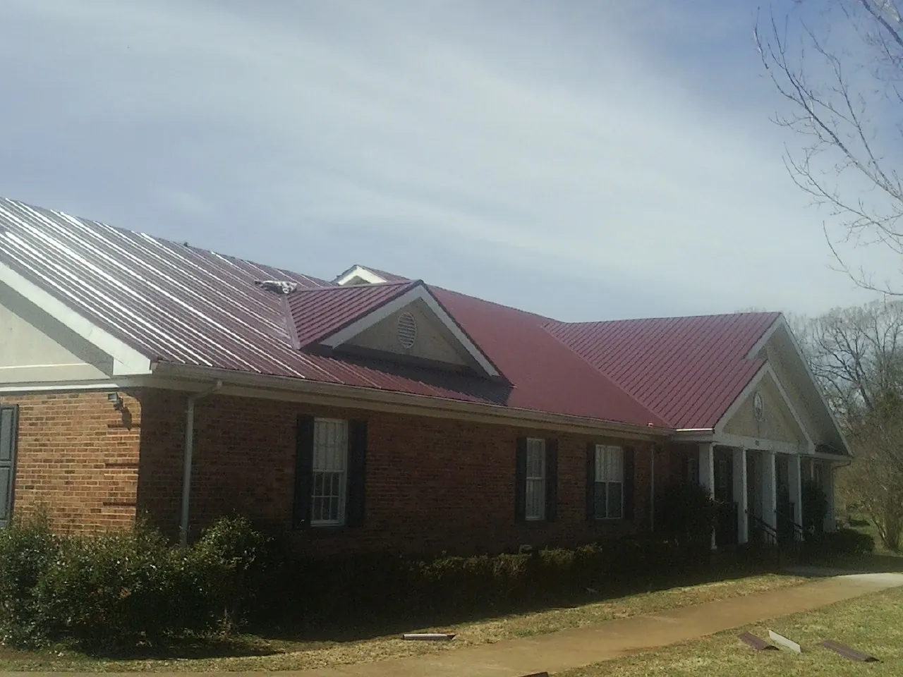 Red metal roof with gabled entries on a long brick building, from a Hail Damage Roof Repair job in Varysburg