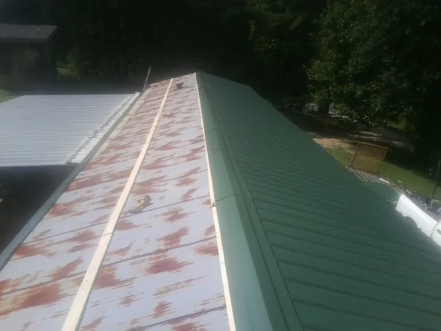Old rusted panels beside newly installed green metal roofing — Wind Damage Roof Repair by Roofing Brothers in Varysburg
