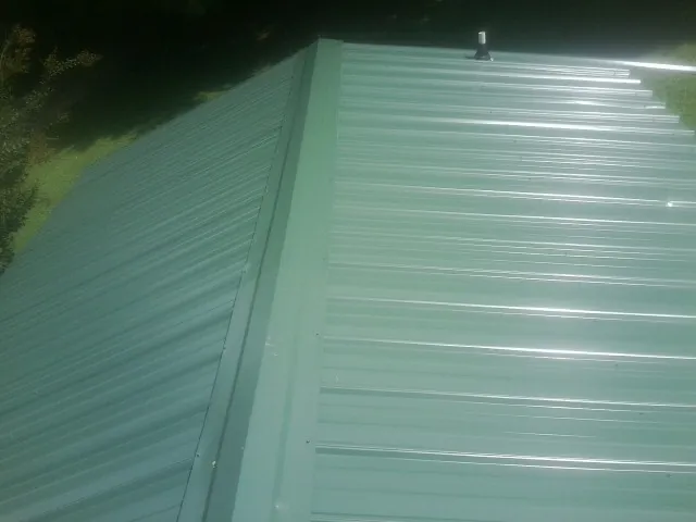 New green metal panels meeting at the ridge of a roof — Flat Roof Repair work by our crew in Varysburg
