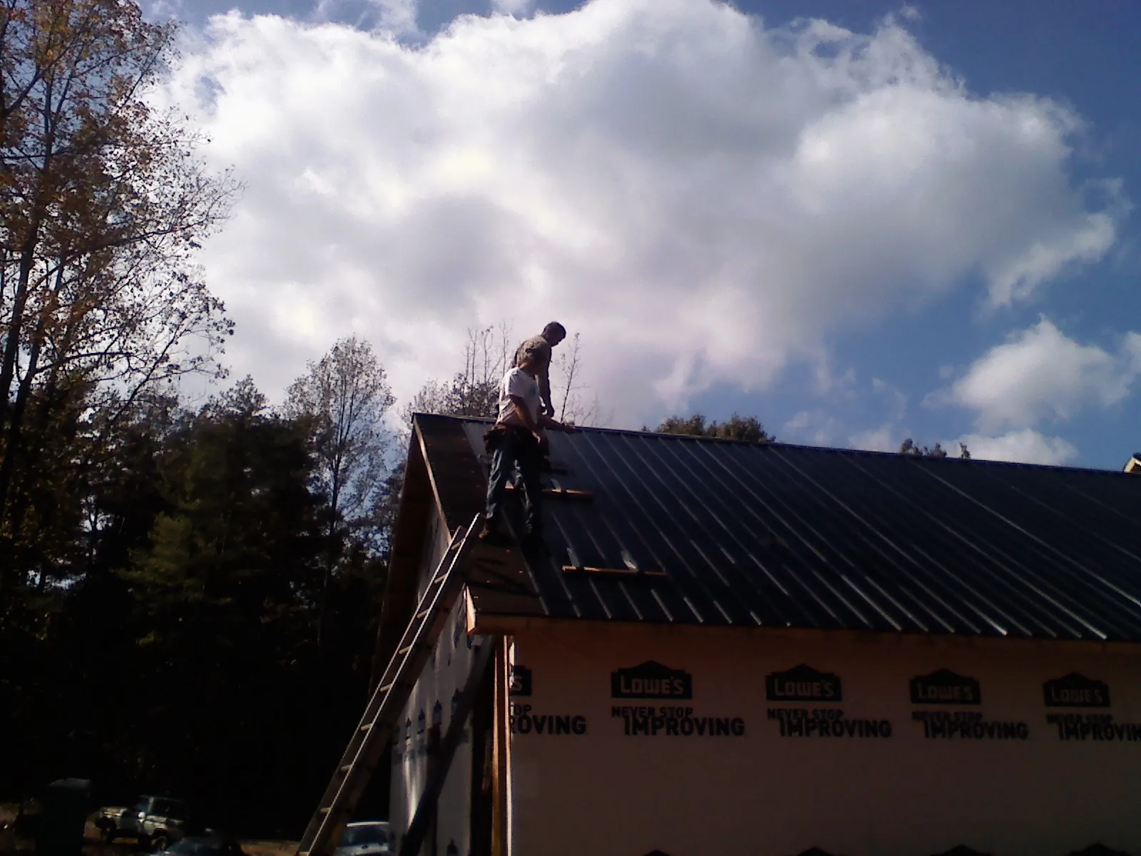 Roofer fastening dark metal panels high against a cloudy sky, from a Roof Inspection job in Varysburg