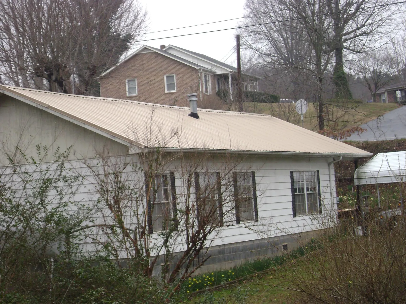 Tan metal roof on a white sided house set into a hillside — Commercial Roofing by Roofing Brothers in Varysburg
